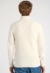 Witte gebreide trui met een ruitpatroon, hoge kraag en geribde manchetten. De textuur lijkt zacht en dik, ontworpen voor warmte.