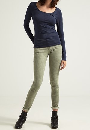 Navy long-sleeve shirt with a scoop neck, paired with olive green skinny pants. Model wears black ankle boots with buckle detail.