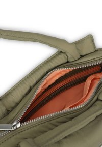 Olivovozelená taška s jemnou textúrou, vybavená zipsovým otvorom, ktorý odhaľuje broskyňovú podšívku a ďalšiu hnedú zipsovú kapsu vo vnútri.