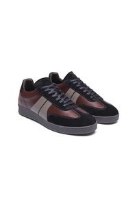 Leather and suede sneakers in black and brown, featuring gray side stripes and flat laces. Rounded toe and rubber sole with visible stitching.