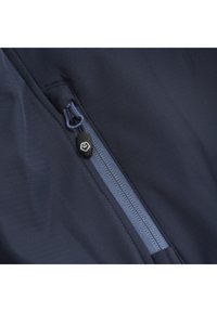 Giacca navy con una superficie testurizzata. Presenta una cerniera visibile di un blu più chiaro e un tirante in gomma nera con un logo.