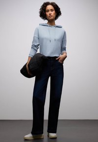 Lyseblå hættetrøje, mørkeblå højtaljede jeans og cremefarvede sneakers, med en sort puffjakke holdt under armen.