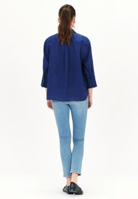 Navyblauwe linnen blouse met lange mouwen, relaxed fit en manchet details, gecombineerd met lichtblauwe jeans en zwarte schoenen. Achteraanzicht weergegeven.