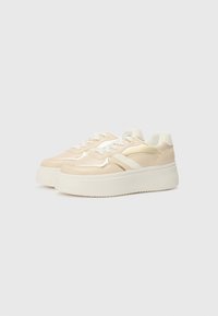 Beige plattformsneakers med en blank finish, med hvite lisser og detaljer. Strukturerte former og polstret krage for komfort.