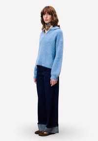 Ein blauer Mohair-Mix-Pullover mit Kragen, kombiniert mit weit geschnittenen, dunklen Denim-Hosen mit kontrastierendem Saum und braunen flachen Schuhen.