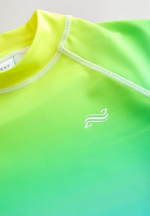 Närbild av en atletisk tröja med en gradient från gul till grön, vita stygn och en liten vit abstrakt logotyp på bröstet.