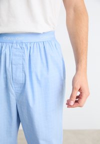 Helleblaue Calvin Klein Boxershorts mit Karomuster, ausgestattet mit einem elastischen Bund mit "Calvin Klein" Logo und Seitentaschen.
