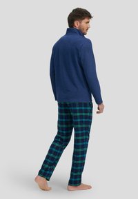 Suéter de hombre en color azul marino con cuello alto, combinado con pantalones de pijama a cuadros en verde y azul. Material de mezcla de algodón, corte relajado, descalzo.