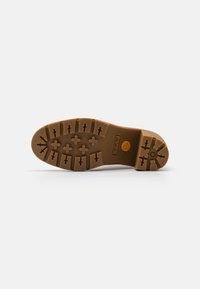 Brown rubber sole with a tread pattern of crosses and arrows. Features a circular logo and a textured band near the edge.