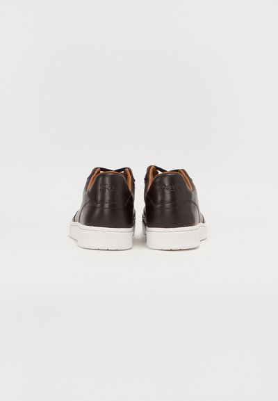 Baskets en cuir marron avec semelles en caoutchouc blanches, présentant une finition lisse, des accents marron contrastants et des éléments de design minimalistes.