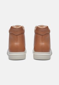 Sneaker high-top in pelle marrone con finitura testurizzata, suola in gomma bianca e design del collare posteriore arrotondato. Cuciture semplici e dettagli.
