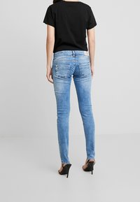Smala blå denimjeans med en urtvättad look, som har två bakfickor och subtila sömnadsdetaljer. Bärs med en svart T-shirt och klackar.
