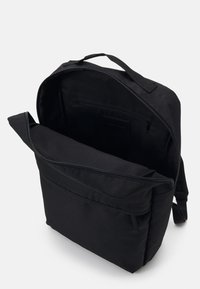 Black fabric backpack featuring a spacious interior with a flat pocket and zip closure. Adjustable straps and top handle included.