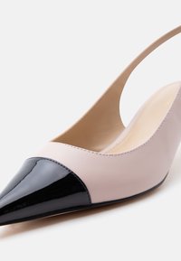 Γυναικείο δίχρωμο γοβάκι slingback με μυτερή μαύρη πατented μύτη και κορυφή από ανοιχτό μπεζ δέρμα σε λευκό φόντο.