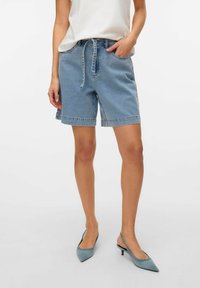 Šviesiai mėlyni džinsiniai šortai su elastinga juostos dalimi ir raišteliu. Įrengti su dviem šoniniais kišenėmis ir kraštu, kuris baigiasi virš kelių.