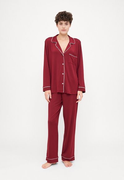 Maroon pajama set made of soft fabric, featuring long sleeves, a pocket on the top, white piping accents, and straight-legged pants.