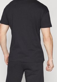 Černé bavlněné tričko s krátkými rukávy, klasickým výstřihem a volným střihem. Hladká textura, jemné švy viditelné podél lemu.