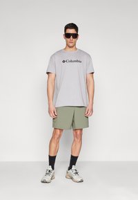 Šedé tričko s krátkým rukávem a černým logem "Columbia", olivově zelené kraťasy, černé ponožky a pestré tenisky. Minimalistický design.