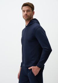 Felpa blu navy realizzata in tessuto morbido, dotata di cappuccio con cordino, maniche lunghe e una vestibilità comoda. Texture liscia senza motivi visibili.