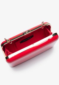 Pochette rigide rouge avec quincaillerie dorée. L'intérieur présente une doublure rouge et une étiquette de marque. Les détails de la fermeture à fermoir sont visibles.