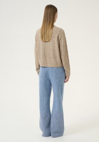 Beige gestrickter Pullover mit einem cropped Design, kombiniert mit hellblauen, ausgestellten Jeanshosen, die ein dezentes vertikales Streifenmuster aufweisen.