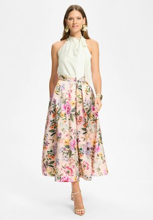 Kobieta w białym, bezrękawnikowym topie na szyję, kwiecistej, wysokiej talii spódnicy midi, złotych kolczykach, bransoletce typu mankiet oraz złotych sandałkach na paski.