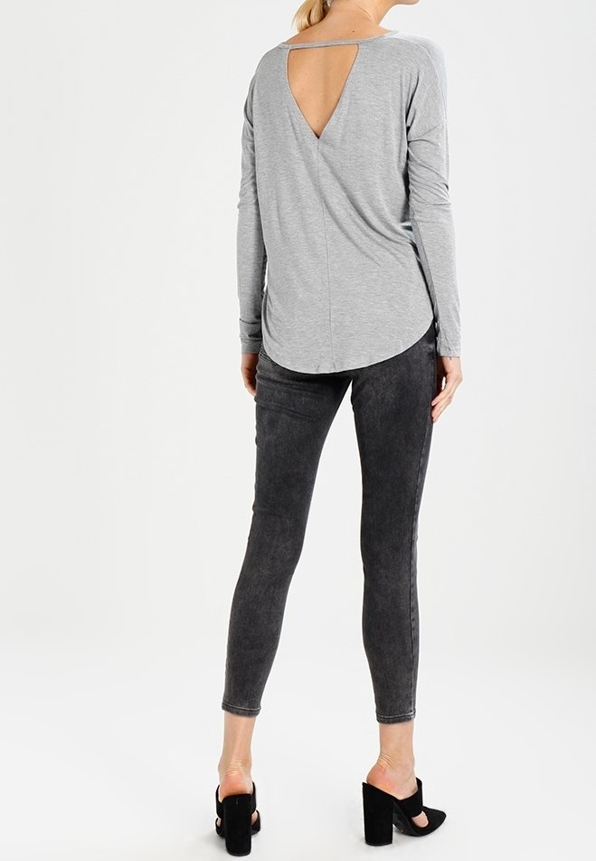 Graues Langarmoberteil mit V-förmigem Rückenausschnitt, kombiniert mit dunkelgrauen Skinny-Jeans und schwarzen Open-Toe-Highheels. Weicher Stoff, figurbetonter Schnitt.