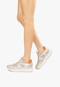 Baskets légères avec une tige en mesh, accents métalliques dorés et blancs, languette de talon orange et semelle blanche épaisse, adaptées à un usage casual.