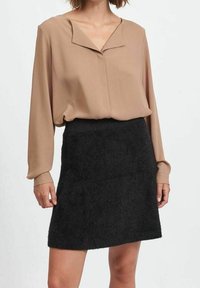 Blusa beige con colletto a V e maniche lunghe, abbinata a una mini gonna nera fluffy, con una silhouette dritta e una texture liscia.