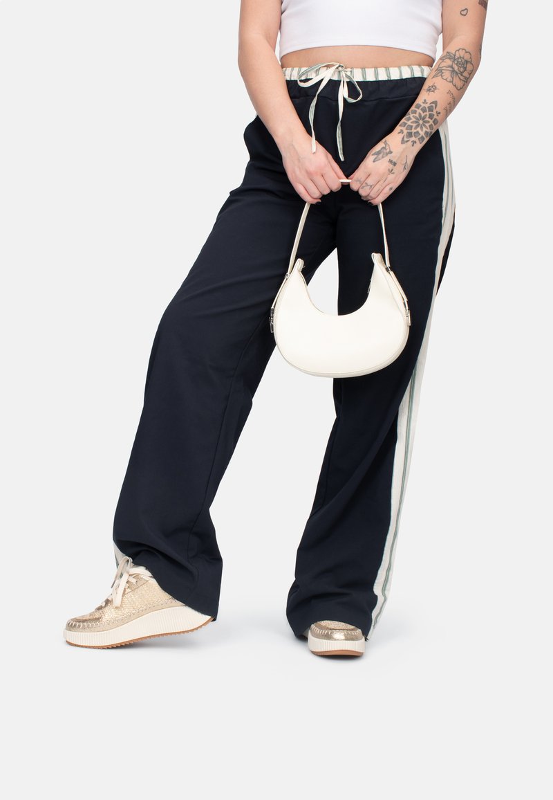 Dunkelblaue weite Hose mit Kordelzugbund und weißen Seitenstreifen. Kombiniert mit metallisch goldenen Sneakern und einer crèmefarbenen Handtasche.