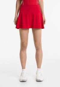Rode tennisrok met een uitlopende snit en een aansluitende tailleband, gemaakt van gladde, rekbare stof, gecombineerd met witte sportschoenen.