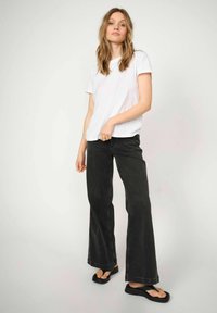Vit kortärmad t-shirt i kombination med svarta utsvängda jeans. Jeansmodellen har hög midja och rå kant. Svarta platta sandaler kompletterar outfiten.