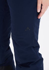 Marinblå utomhusbyxor med mjukt, texturerat tyg, ergonomisk design och en svart logotyp på nedre benet.