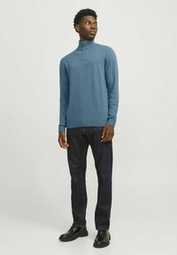 Sudadera de cremallera azul oscuro con mangas largas, puños y dobladillo acanalados, combinada con jeans oscuros y zapatos negros de cordones. Tejido de punto suave.