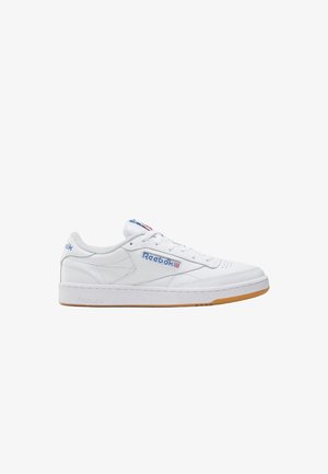 Witte lage Reebok sneaker met blauw logo, Union Jack vlagdetails, witte veters en gum rubberen zool op een effen witte achtergrond.
