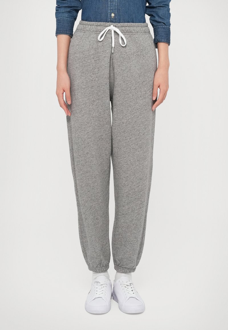 Sivé tepláky s elastickými manžetami a šnúrkou v páse. Vyrobené z mäkkej látky, majú bočné vrecká. Nosené s bielou obuvou.