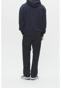 Marineblauer Hoodie mit Kängurutasche, kombiniert mit schwarzen, leichten Hosen und Sneakers mit blauen und weißen Akzenten. Minimalistisches Design.