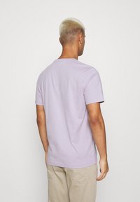 Camiseta de algodón color lavanda con escote redondo y mangas cortas, diseño liso y ajuste regular, vista desde atrás.