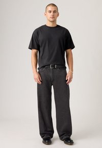 Black cotton t-shirt with short sleeves, paired with loose-fitting, dark gray denim jeans and a black belt. Simple, casual design.