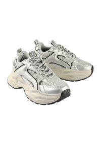 Stříbrné sportovní tenisky s síťovinou a syntetickými překryvy, s robustní krémovou mezipodešví, černou podešví a výraznými logovými akcenty.