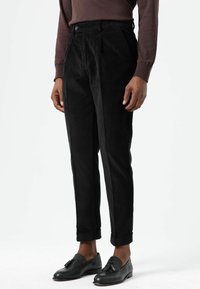 Zwarte corduroy broek met rechte pasvorm, geplooide voorkant en omgeslagen pijpen, gecombineerd met zwarte loafers.