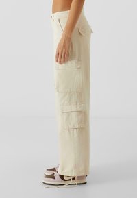 Lys beige cargo-bukser med flere lommer, rett snitt og en lett tekstur. Brukt med lave sneakers i rosa og brune aksenter.