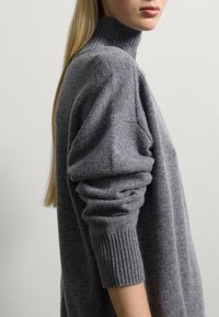 Grauer Rollkragenpullover aus weichem, strukturiertem Strickstoff. Mit einem lässigen Schnitt, gerippten Bündchen und einem hohen Kragen.