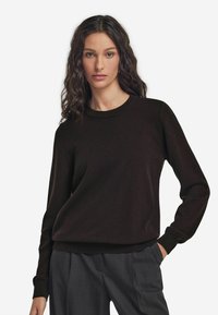 Czarny sweter dzianinowy z okrągłym dekoltem, ściągaczami na mankietach i u dołu, charakteryzujący się luźnym krojem. Noszony na szarych spodniach, ukazujących gładką teksturę.