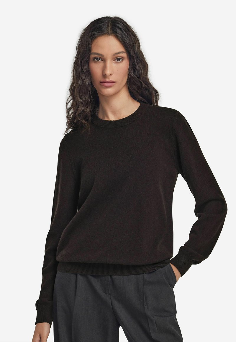 Czarny sweter dzianinowy z okrągłym dekoltem, ściągaczami na mankietach i u dołu, charakteryzujący się luźnym krojem. Noszony na szarych spodniach, ukazujących gładką teksturę.