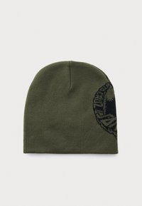 Olijf groene gebreide beanie met een gedeeltelijk zwart cirkelvormig grafisch ontwerp aan de zijkant, weergegeven op een witte achtergrond.