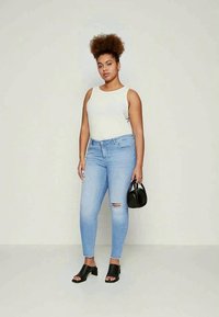 Šviesiai pilkas atidengtas marškinėliai, nusidėvėję šviesiai mėlyni džinsai, juodi atvirų pirštų blokiniai aukšti kulniukai ir mažas juodas rankinukas.