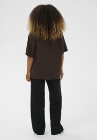 T-shirt oversize marrone con maniche corte, abbinato a pantaloni neri larghi. Tessuto dalla superficie liscia, design semplice e minimalista.