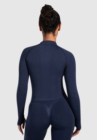 Bodysuit deportivo de manga larga en color navy con textura acanalada, diseño ajustado y cuello alto. Su construcción sin costuras realza la forma del cuerpo.