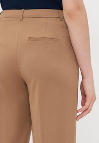 Bruine op maat gemaakte broek met een gladde textuur, met een enkele achterzak en riemlussen in de tailleband.